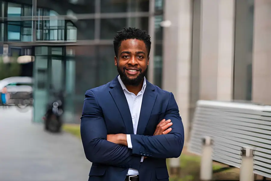 Confident young professional in a navy blazer with arms folded outside an office building