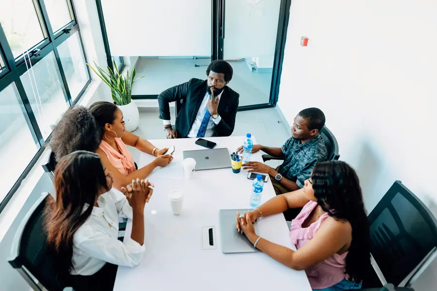 A tutor in a suit leads a discussion with four students around a white table